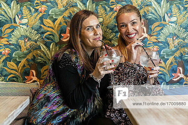Porträt zweier erwachsener Frauen  die am Restauranttisch einen Cocktail genießen