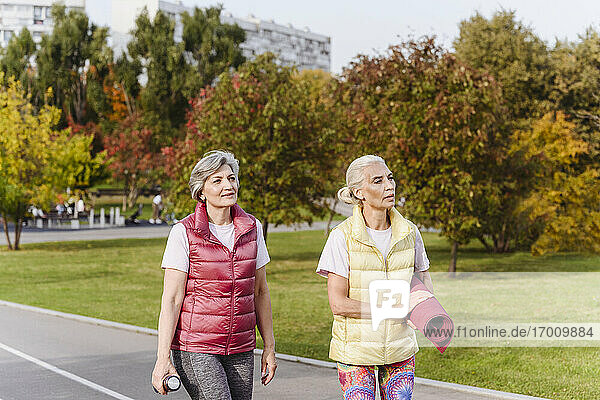 Freundinnen beim Spazierengehen mit Trainingsmatte in einem öffentlichen Park