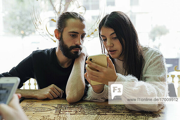 Junge Freunde benutzen ihr Smartphone  während sie im Restaurant sitzen