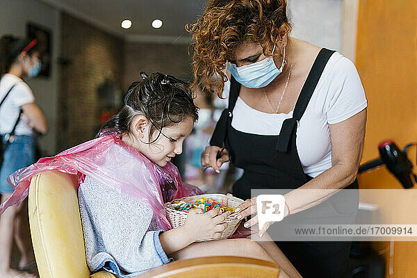 Friseurin und Mädchen suchen im Korb mit Haarspangen beim Friseur während des Coronavirus