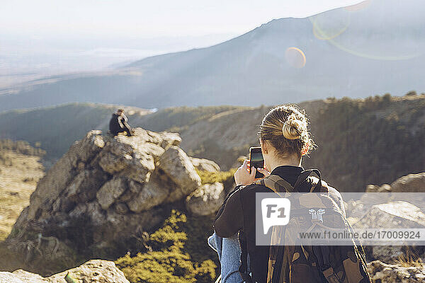 Junge Frau fotografiert männlichen Freund auf dem Gipfel eines Berges sitzend