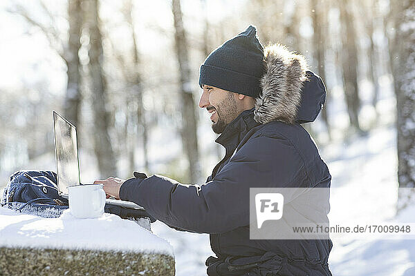 Lächelnder Geschäftsmann bei der Arbeit am Laptop im Schnee Sonnenlicht