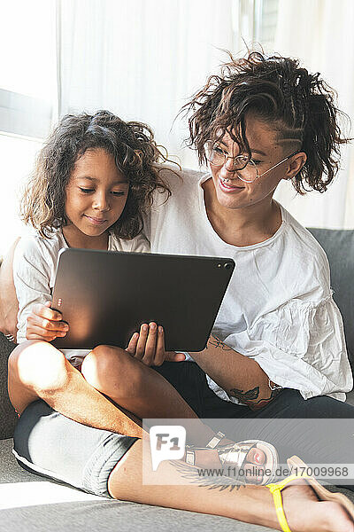 Mother and daughter sitting together on sofa with digital tablet