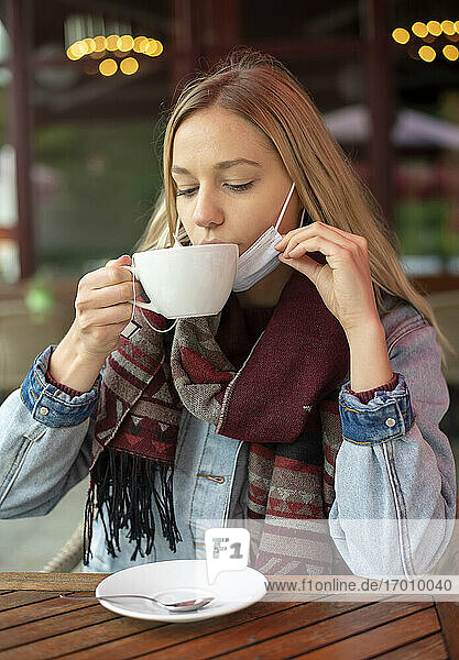 Junge Frau trinkt Tee in einem Restaurant während einer Pandemie
