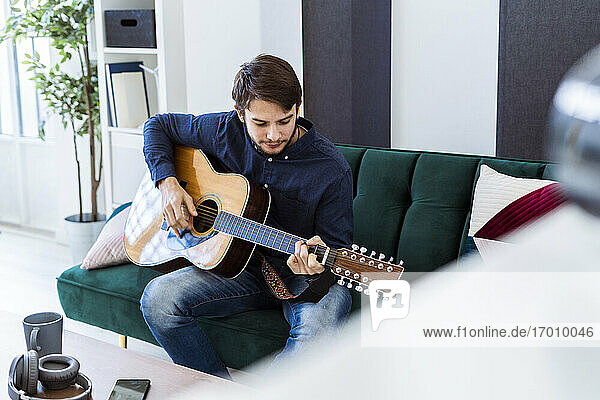 Musician playing guitar while sitting on sofa at studio