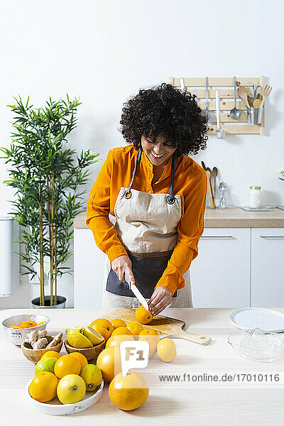 Junge Frau schneidet eine Orange für die Herstellung von Saft  während sie in der Küche zu Hause steht