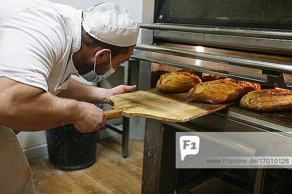 Männlicher Bäcker nimmt Brote aus dem Ofen in der Küche einer Bäckerei