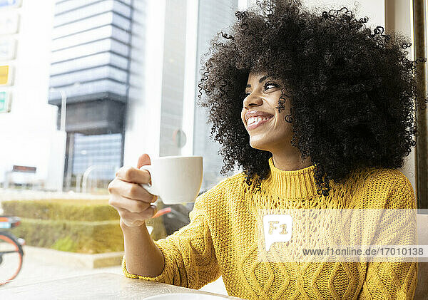 Lächelnde Frau  die wegschaut  während sie in einem Café sitzt und Kaffee trinkt