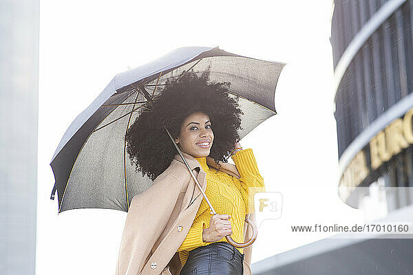 Lächelnde Frau mit lockigem Haar  die eine Kamera hält  während sie im Freien steht