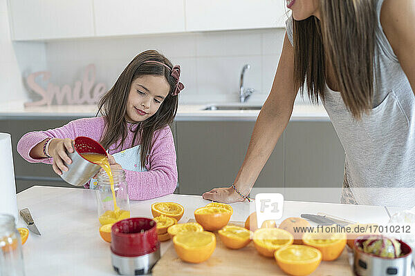 Tochter gießt Orangensaft in ein Glas und steht neben ihrer Mutter in der Küche
