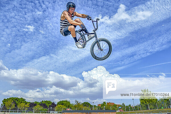 Unbekümmerter Mann mit Fahrrad  der gegen den blauen Himmel im Fahrradpark springt