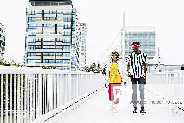 Mittlere erwachsene Frau und Mann unterhalten sich beim Gehen auf einer Brücke in der Stadt