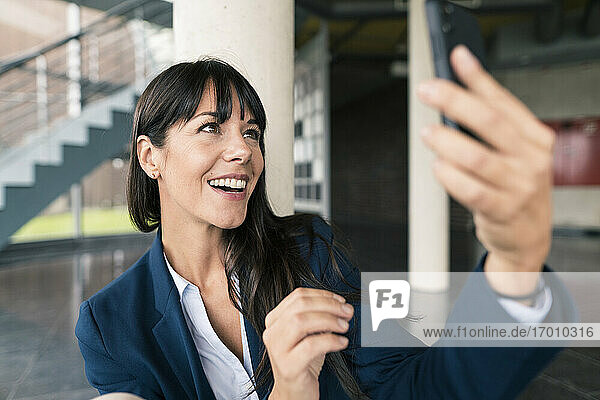 Lächelnde Unternehmerin bei einem Videoanruf über ein Smartphone in der Lobby