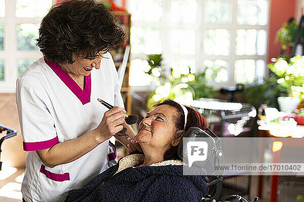 Lächelnde Krankenschwester beim Schminken einer behinderten Frau im Pflegeheim