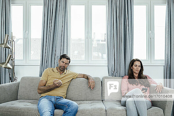 Mature woman using phone while man looking at nails at home