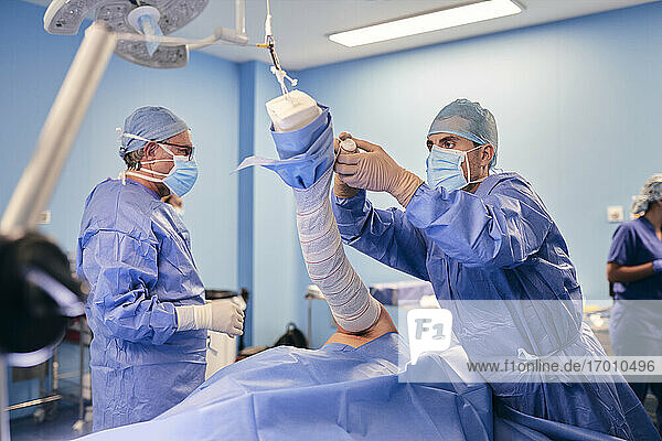 Arzt wickelt Hand  während er mit einem Kollegen im Hintergrund im Operationssaal steht