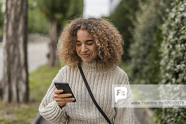 Smiling young woman text messaging through smart phone in city