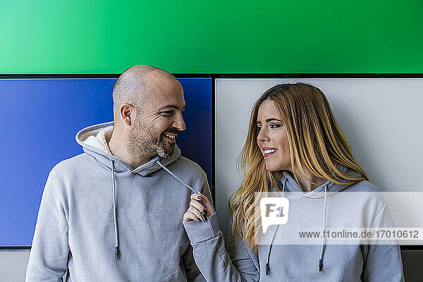 Smiling couple looking at each other while standing against colorful wall