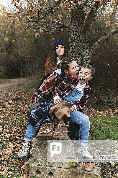 Drei lächelnde Schwestern auf einer Bank in einer Herbstlandschaft