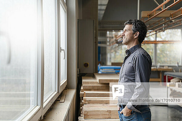 Porträt eines Zimmermanns  der durch ein Fenster in einer Produktionshalle blickt