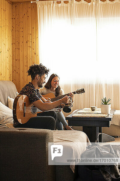 Mann und Frau spielen Gitarre  während sie zu Hause auf dem Sofa sitzen