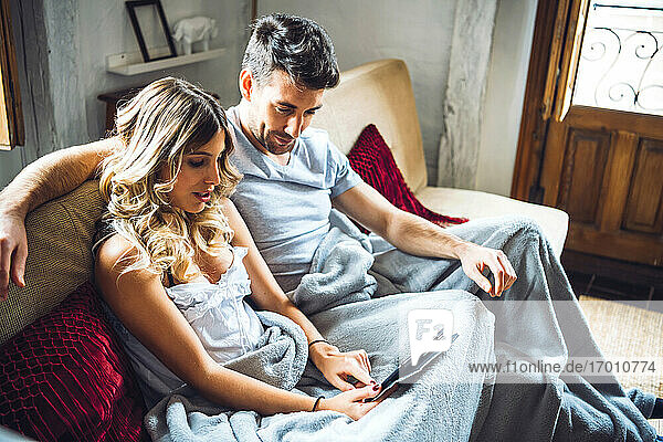 Junges Paar kuschelt auf der Couch zu Hause und schaut Tablet