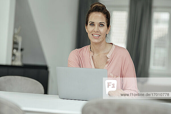 Glückliche Unternehmerin mit Laptop am Tisch im Heimbüro