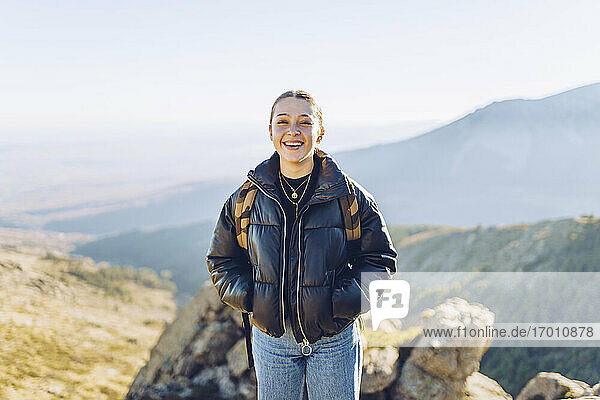 Lächelnde junge Frau auf einem Berg stehend gegen den Himmel an einem sonnigen Tag