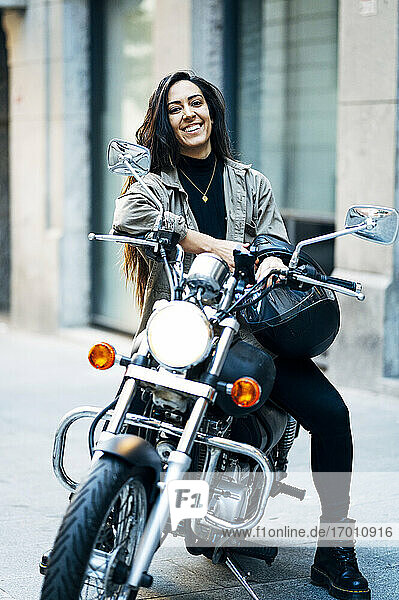 Glückliche Motorradfahrerin mit Helm auf einem Motorrad sitzend in der Stadt