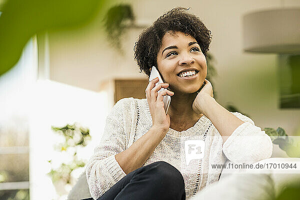 Junge Frau  die zu Hause sitzend mit ihrem Handy telefoniert