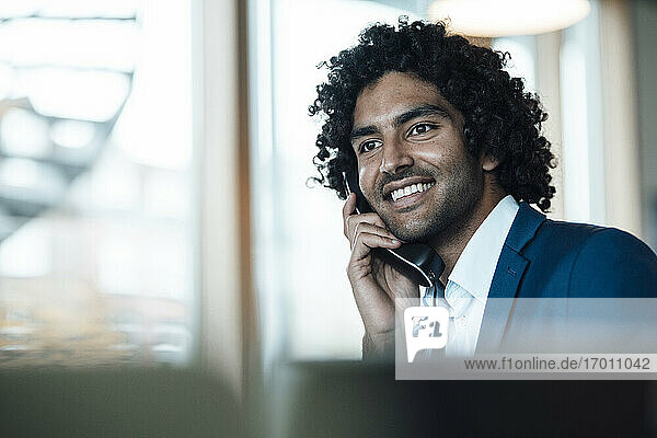 Lächelnder junger Mann  der am Festnetztelefon spricht und seinen Blick vom Arbeitsplatz abwendet
