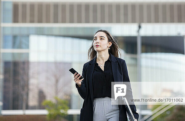 Junge Geschäftsfrau mit Laptop und Mobiltelefon beim Spaziergang im Freien