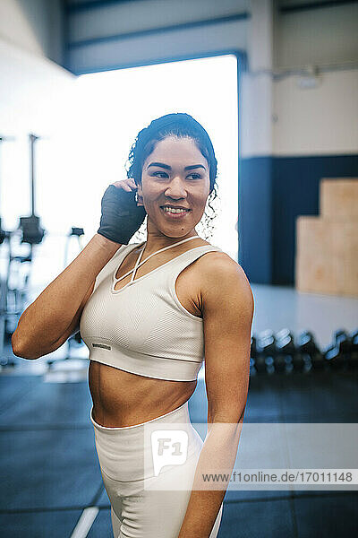 Lächelnde Sportlerin mit Hand im Haar träumt im Fitnessstudio