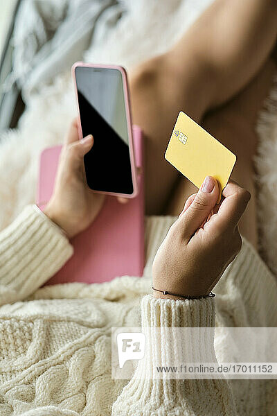 Frau kauft zu Hause online mit Kreditkarte über ihr Smartphone ein