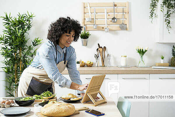 Junge Frau benutzt ein digitales Tablet  während sie in der Küche vegane Sandwiches zubereitet