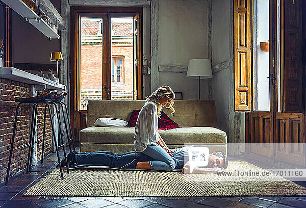 Junge Frau massiert ihren Freund auf dem Teppich im Wohnzimmer zu Hause
