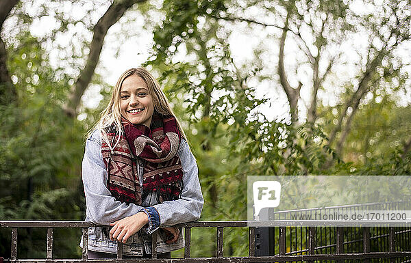 Lächelnde Frau lehnt an einem Geländer in einem herbstlichen Park