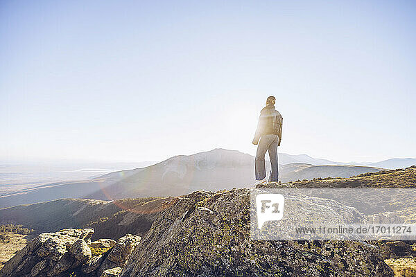 Weibliche Wanderin steht auf dem Gipfel eines Berges gegen den klaren Himmel an einem sonnigen Tag