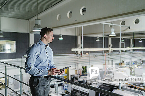 Geschäftsmann mit digitalem Tablet mit Blick auf eine Fabrikhalle