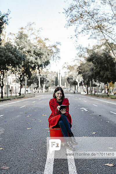 Junge Frau in roter Jacke benutzt ein digitales Tablet  während sie auf einem Stuhl an der Straße sitzt