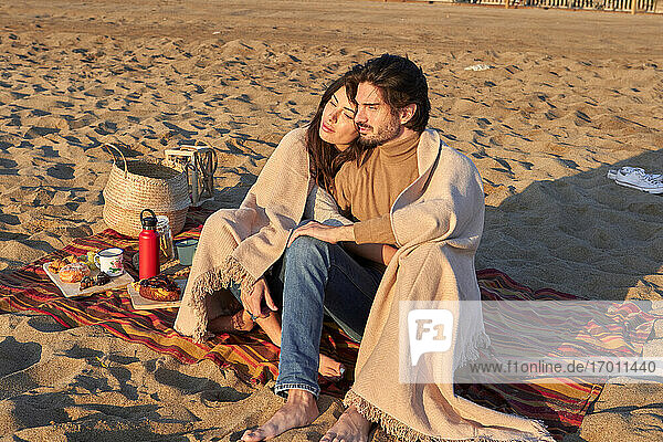 Junges Paar mit Decke  das am Strand sitzt und sich ausruht