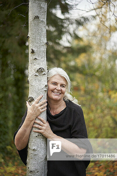 Happy senior woman hugging tree trunk in autumn park