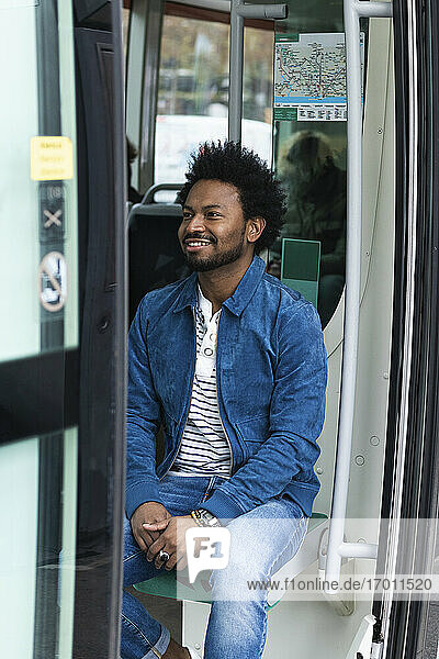 Stilvoller erwachsener Mann mit Afro-Haar  der in einem Bus sitzt  gesehen durch eine Türöffnung