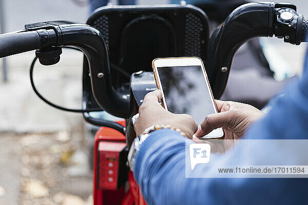 Hände eines Mannes  der sein Smartphone benutzt  um an einer Parkstation ein Fahrrad zu mieten