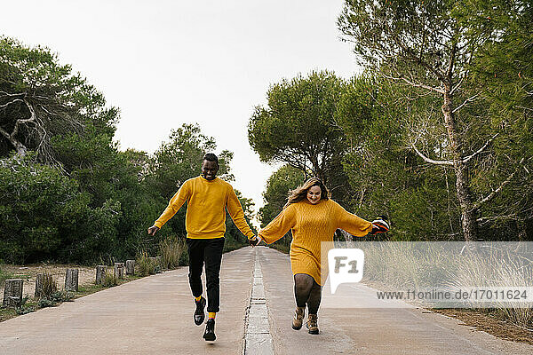 Carefree couple holding hands while running on road