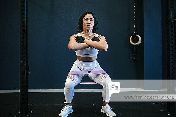 Sportswoman with resistance band in gym against wall