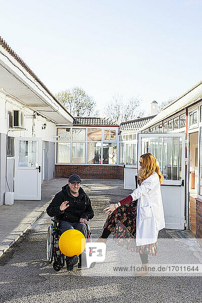 Ein behinderter Mann und eine Krankenschwester spielen mit einem Ball vor einem Rehabilitationszentrum
