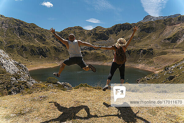 Paar hält sich an den Händen  während es an einem sonnigen Tag über einen Berg springt