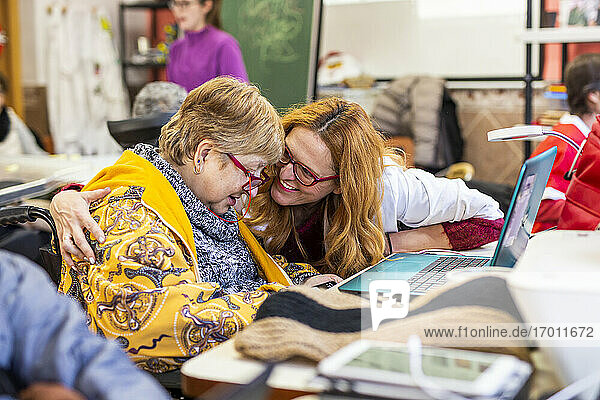 Lächelnde Betreuerin im Gespräch mit einer behinderten Frau am Laptop im Rehabilitationszentrum