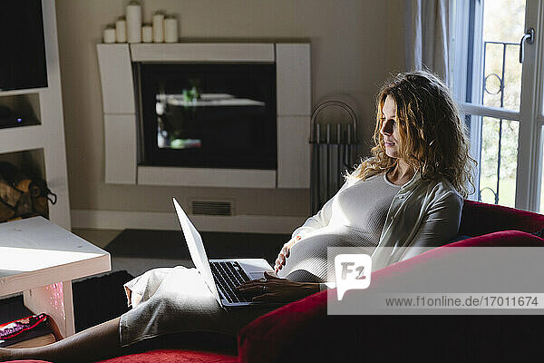 Pregnant freelancer using laptop while sitting on sofa in living room